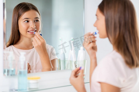 美容和化妆品概念—少女应用唇膏和寻找镜子在家庭浴室。十几岁的女孩应用唇膏在浴室