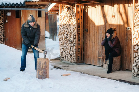 男装冬装摄影照片_一个穿着冬装的家伙在院子里劈柴，覆盖着雪