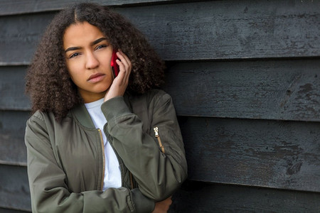 青少年脊椎侧弯摄影照片_美丽的混血黑人女孩十几岁的女青年在外面看起来悲伤、沮丧或若有所思地打手机