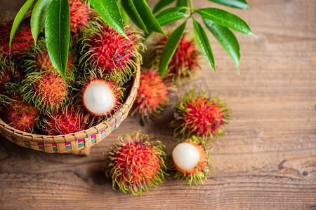 红毛丹水果放在篮子里，木质背景从花园里收获，新鲜成熟的红毛丹甜蜜的热带水果剥了红毛丹的叶子