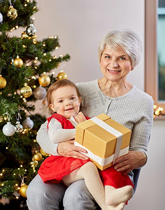 圣诞节，节日和家庭概念-快乐的祖母和小孙女在家里带着礼物。祖母和女婴带着圣诞礼物