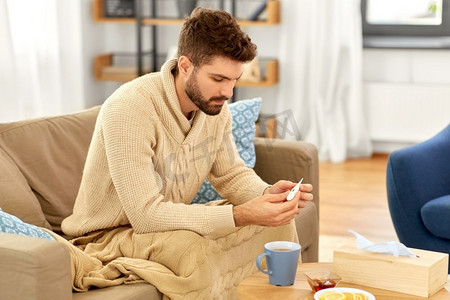 人，健康和发烧概念—生病的人在毯子测量温度由温度计在家里。病人用温度计测量体温