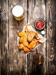烟熏鸡翅配啤酒和酱汁。在一张木桌上。烟熏鸡翅配啤酒