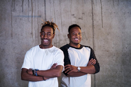 成立社团摄影照片_两名年轻的非裔美国人微笑的休闲商人站在新成立的办公室的水泥墙前的肖像