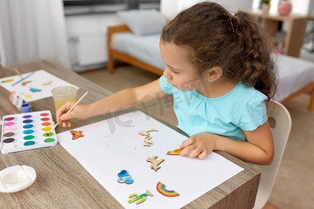 简笔画手摄影照片_童年，爱好和休闲概念—小女孩用画笔画木纸板项目在家里。小女孩在家里画木制物品