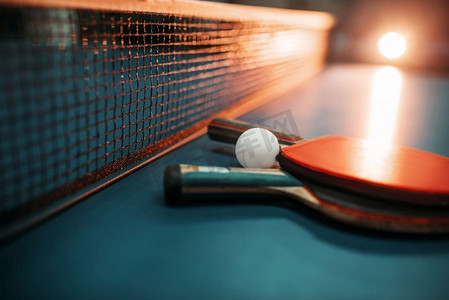 运动乒乓球摄影照片_两个网球拍和球网放在桌子上，比赛理念。乒乓球运动器材。两个网球拍和桌子上的球对网