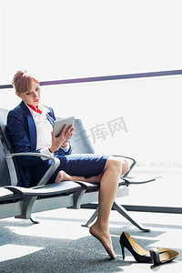 年轻美丽的机场工作人员使用数字平板电脑，而坐在椅子上休息