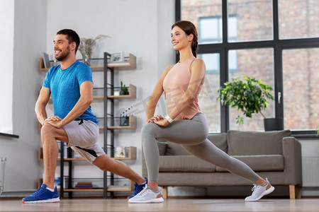 运动，健身，生活方式和人们的概念—微笑的男人和女人在家里锻炼和做弓步。夫妇锻炼和做弓步在家里