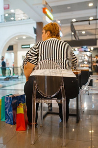 胖女人坐在快餐店的桌子上，背影。在商场快餐店超重的女性，肥胖问题