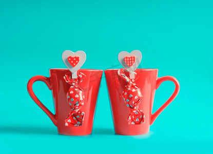 情人巧克力摄影照片_两个红色茶杯与巧克力果仁糖和心在蓝色背景。情人节和爱情的概念。前视图。