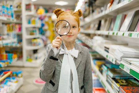 小女生选择放大镜，在文具店购物。女孩子在商店买办公用品，学童在超市