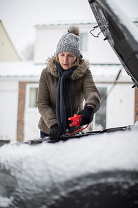 雪天，一名女子在汽车电池上使用跳线电缆