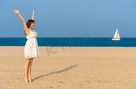站在海滩上庆祝手臂在海滩上举起的年轻女子或女孩，背景是一艘在海上航行的白色游艇或帆船