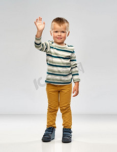穿着衬衫的手摄影照片_童年与人的概念--穿着条纹衬衫的小男孩在灰色背景上挥手。穿条纹衬衫的小男孩挥手