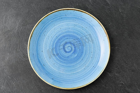 陶瓷器皿摄影照片_餐桌摆设、餐具和餐饮理念-板岩背景下蓝色陶瓷板的特写。板岩背景上的蓝色陶瓷板特写