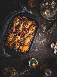 美味的烤鸡腿配红洋葱和葡萄，在铸铁砂锅锅里，黑色乡村背景，俯视