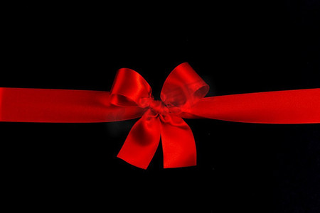 圣诞红摄影照片_在黑色纸背景的红缎丝带蝴蝶结。红色蝴蝶结黑色