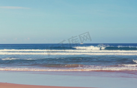 海洋模糊摄影照片_海滩上的蓝色波浪。模糊的背景和阳光斑点。宁静的自然背景。
