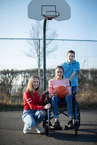 肖像的青少年女孩在轮椅上打篮球与朋友