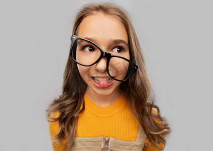 高中，教育和视觉概念-在灰色背景下戴着眼镜微笑的十几岁女学生。戴着眼镜微笑的十几岁女学生