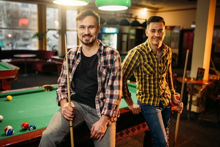 两个男性台球选手与线索摆在桌子上与彩色球，台球室。男子在体育酒吧玩美国台球游戏