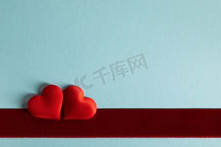 情人节两个红色丝绸心和红色缎子丝带在蓝色纸背景，爱概念。’情人节红心在蓝色