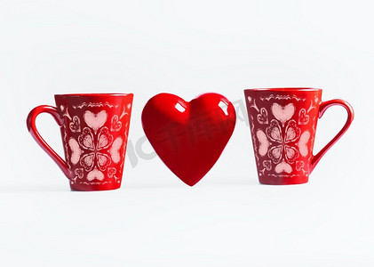 对党摄影照片_两个红色杯子与心脏装饰站在白色背景。创意情人节或爱情概念