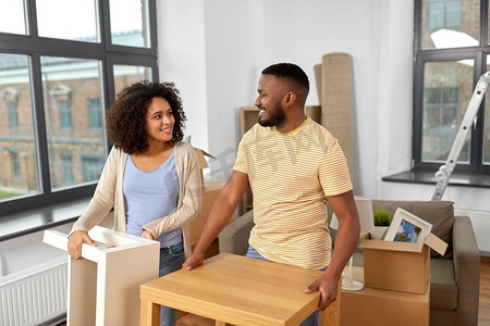 搬家，人员，维修和房地产概念-幸福的非裔美国夫妇在新家有桌子的东西。喜结良缘的夫妻搬进新家