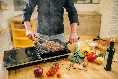 男人在厨房的平底锅里煮肉。男人准备煮猪肉在桌上电炉