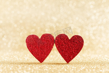 在明亮的金色灯光下，两个手工制作的小红心闪闪发光，背景是情人节卡片。波克背景上的两颗心