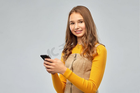与人连接摄影照片_科技、沟通与人的概念--微笑的少女在灰色背景下使用智能手机。微笑的少女使用智能手机