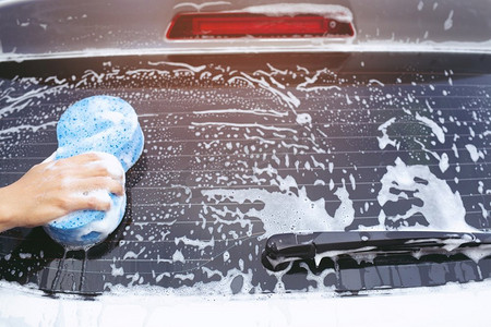 洗车汽车摄影照片_人们手持蓝色海绵洗车。