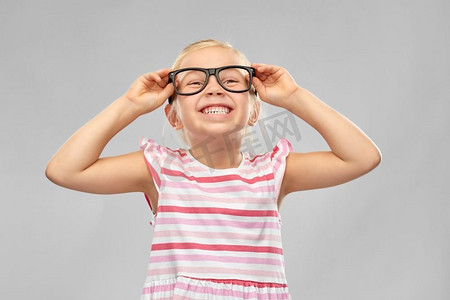 教育、学校和视觉概念-灰色背景下戴着黑色眼镜的可爱小女孩微笑。戴着黑眼镜微笑的可爱小女孩