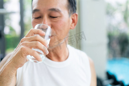 喝矿泉水摄影照片_老年人运动后到健身中心喝矿泉水。老年人健康的生活方式