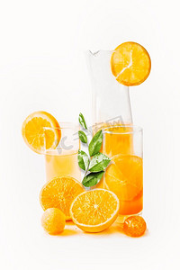 维生素c摄影照片_橙汁在玻璃杯和壶与切片和绿叶在白色背景。健康饮料夏季饮料令人耳目一新。维生素c