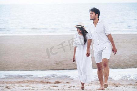 在蜜月旅行假期期间走在海滩上的愉快的年轻夫妇。幸福的年轻夫妇在蜜月的海滩上散步。