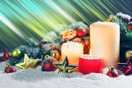 点燃的圣诞蜡烛上点缀着红色和金色的装饰星、小玩意儿、松果和雪地上的绿色树枝。带装饰品的圣诞蜡烛