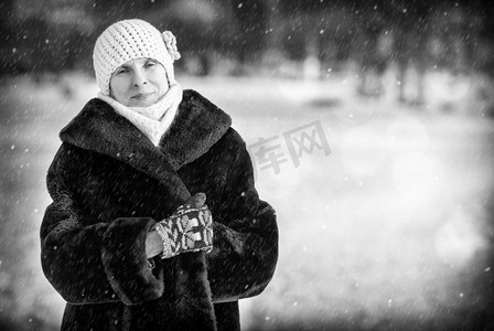 女士冬季帽子摄影照片_一幅面带微笑的老年成年妇女的冬季肖像，戴着羊毛帽、围巾和彩色手套，背景是雪地