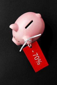 购物，销售和储蓄概念—储蓄罐与百分之七十折扣红色标签在黑色背景在黑色上有红色销售标签的小猪储蓄罐
