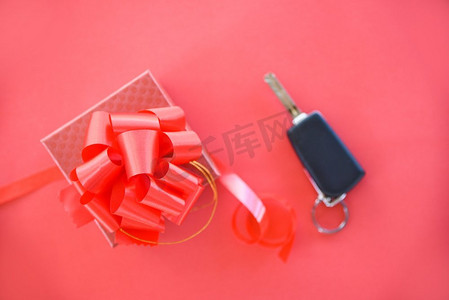 赠送汽车钥匙概念/红色礼盒，红色彩带蝴蝶结和钥匙汽车作为礼物在红色背景上