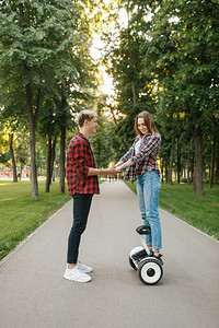 男朋友教他的女孩骑陀螺板在夏季公园。户外娱乐与电动陀螺板。平衡技术运输