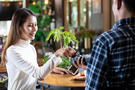 轻扫摄影照片_亚洲妇女顾客使用在信用卡阅读器EDC机的信用卡刷卡支付服务员咖啡购买在咖啡馆的桌子