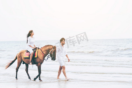 蜜月假期摄影照片_在蜜月旅行假期期间走在海滩上的愉快的年轻夫妇。年轻夫妇在热带海滩骑马。