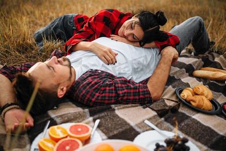 情侣躺在格子布上，在夏天的田野野餐。浪漫的男女之旅。爱的夫妇躺在格子，野餐在夏天的领域