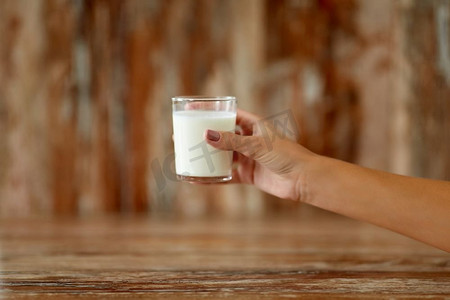 食物，吃和奶制品概念—女性手拿着牛奶的玻璃特写镜头。关闭的女性手拿着杯牛奶