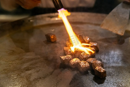 燃烧器摄影照片_烹饪牛肉铁板烧食谱日本烤牛肉在烹饪锅与刮刀和燃气燃烧器火焰