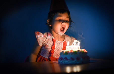 亚洲儿童吹蜡烛在生日蛋糕/小漂亮的女孩的画象生日快乐聚会在晚上
