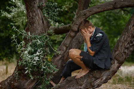 一个穿着破西装坐在荒岛上的树上的紧张商人。商业风险、倒闭或破产概念