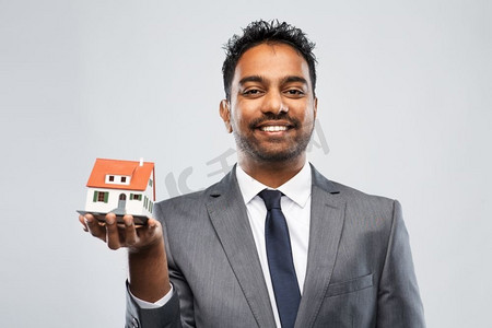 房地产企业摄影照片_房地产企业和人概念—印度人房地产经纪人有房子模型在灰色背景印度人房地产经纪人与房子模型和文件夹