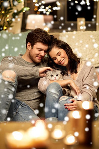 宠物，圣诞节和人的概念—快乐的夫妇与猫在家里超过雪。快乐的夫妇与猫在家里